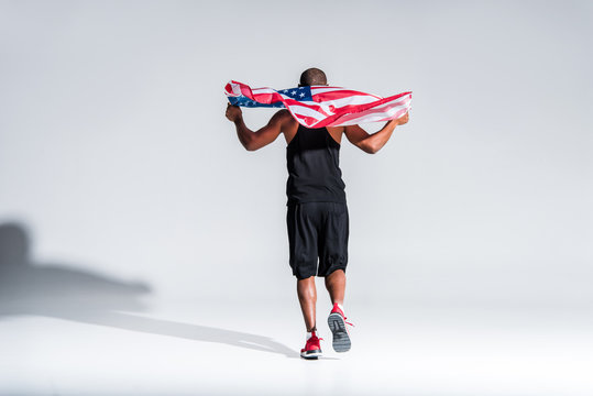 back view of young african american sportsman holding american flag on grey - Powered by Adobe