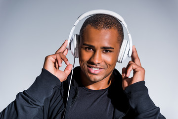 handsome young african american sportsman listening music in headphones and smiling at camera isolated on grey