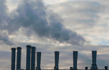 Smoke comes from industrial pipes against a cloudy sky.