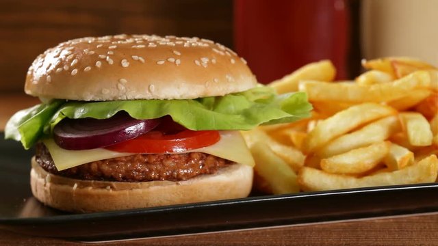Camera moves in front of a fresh hamburger and fries on black plate