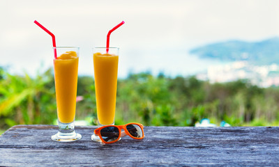 Two glasses of mango cocktail juice and orange sunglasses on wood table. Blue sea on the...