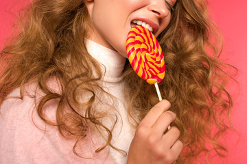 Cropped image of beautiful woman biting lollipop on red