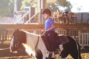 Portrait of little boy riding a horse. First lessons of horseback riding.