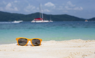 Orange sunglasses on white ocean beach under blue sky. Azure Turquoise Sea in the background. Summer holiday relax background with copy space.
