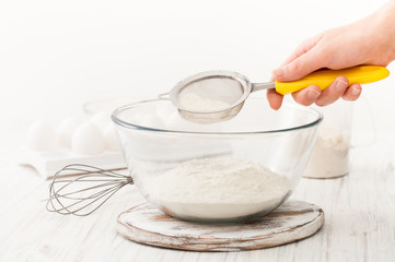 Fototapeta na wymiar Sifting flour into a Cup on a white table in the kitchen