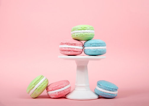 Large Macaroon cookies covered in granulated sugar on a pedestal and table. Pink background. Popular pastry in France.