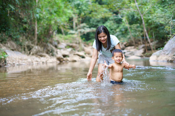 Asian mother in blue shirt with DIY chest pocket playing water with her son about 1 year and 9 months at  waterfall