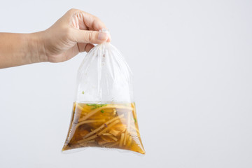 Hand holding boiled braised fish maw in red gravy with blood soup, peppers in plastic bag wrapped by rubber band, A Thai Chinese food