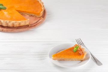 Pumpkin pie Homemade dessert Autumn delicious. Piece of traditional cake with cut pumpkin on white wooden background. Vegetarian food. Horizontal banner for thanksgiving, fall congratulation card