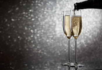 Picture of bottle with flowing champagne in wine glasses on gray background