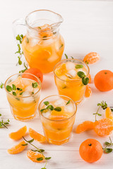 Mandarin cocktail with ice and mint in beautiful glasses and jug, fresh ripe citrus on white wooden background. Sweet orange juice. Close up photography. Selective focus