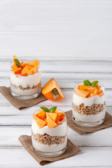 Persimmon creamy trifle in beautiful glasses, fresh ripe fruit slices on white wooden background. Healthy vegetarian food. Delicious dessert. Close up photography. Selective focus.