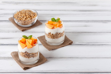 Persimmon creamy trifle in beautiful glasses, fresh ripe fruit slices on white wooden background. Healthy vegetarian food. Delicious dessert. Close up photography. Selective focus.