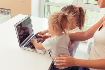 Young happy family using laptop while sitting at kitchen at home. Little children girl watching cartoons with parents
