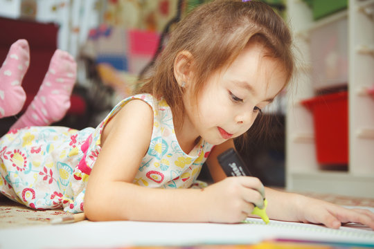 Little girl carefully draw picture in notebook with felt pen