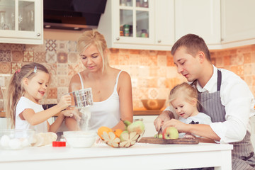 Parents and their two beautiful and cute children girls preparing breakfast ot lunch at kitchen table at home