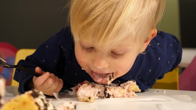 Two years child boy funny eating birthday cake lapping tongue face smeared with sweet cream