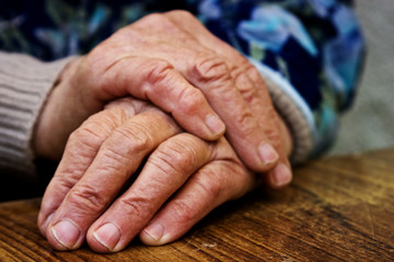 Fototapeta premium Hands of an old grandmother with wrinkles on a wooden table close-up