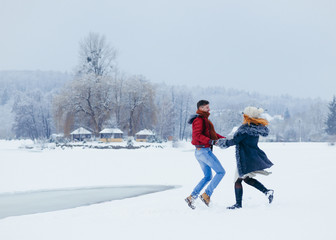 Two cheerful lovers are holding hands and joyfully dancing on the snow in the countryside. Christmas time.