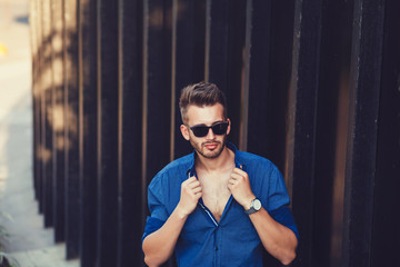 Handsome man in shirt and stylish sunglasses posing near white wall with copy space area for advertising fashion clothing content