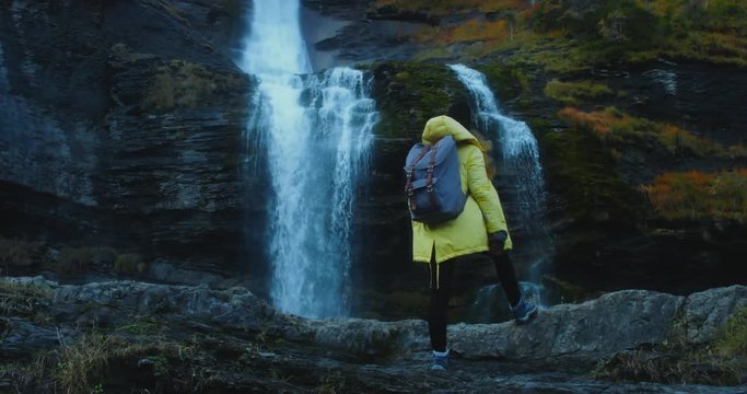 CINEMAGRAPH - SEAMLESS LOOP. Caucasian female hiker in yellow raincoat enjoys the view of a beautiful waterfall in French Alps