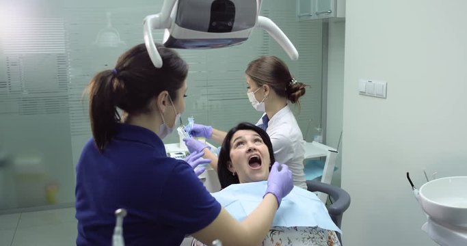 Dentist make a checkup and dental cleaning for a young woman , dental nurse are beside