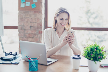 Portrait of happy smiling glad secretary who typing sms on her smartphone instead of working, she...