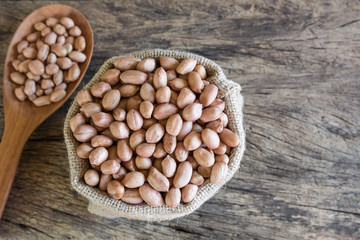 top view of raw dried peanut seeds in a sack bag with ladle on old and crack wooden board with copy space for text.
