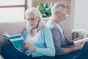 Lovely couple of old wife and husband are reading book with glasses, sitting on a couch at nursing home