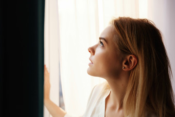 Sun shines over a face of beautiful woman standing before bright window