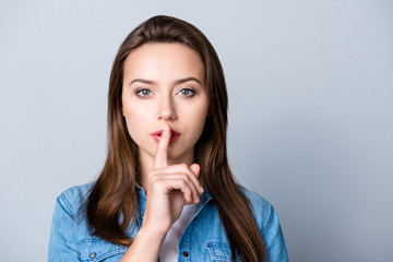 Silence, please! Close up portrait of  young woman holding her forefinger on lips showing hush...