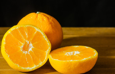 Ripe Mandarin fruit peeled open and place on old rustic look timber with group of mandarin fruits out of focus on the background