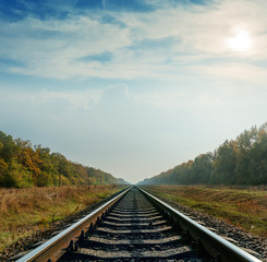 Fototapeta premium railroad closeup goes to horizon under cloudy sky with sun