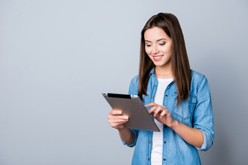 Close up portrait of smiling successful woman in casual outfit looking at her tablet and typing sms through 3g internet while standing over grey background © deagreez