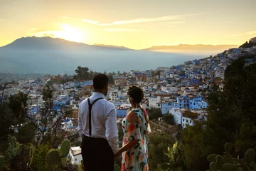 Fotobehang Man and woman hold their hands together wathcing the sunset over the city in Morocco © IVASHstudio