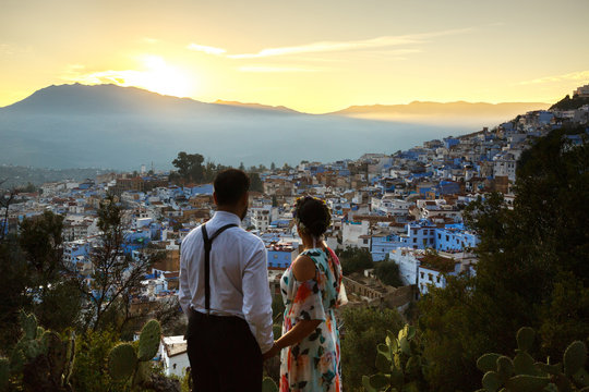 Man and woman hold their hands together wathcing the sunset over the city in Morocco