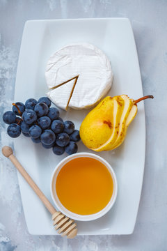 Cheese brie (camembert) with honey and fruits on a white plate.
