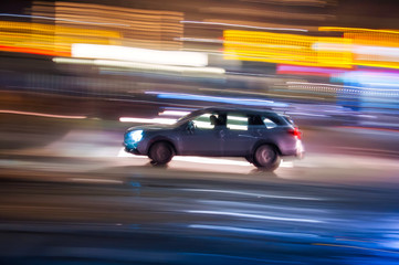 Automobile che sfreccia veloce di notte per le vie con luci colorate di una  grande città 
