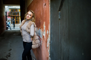 Obraz premium Blonde girl at fur coat posed against old orange wall.