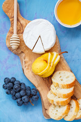 Brie cheese (camembert) with honey, nuts and fruits on a wooden board.