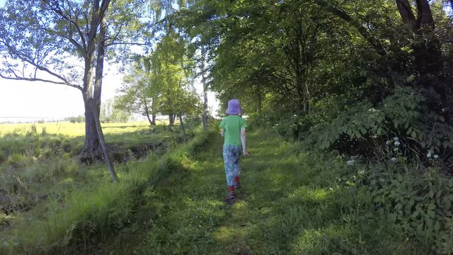 Little girl walking on green footpath. Summer lifestyle moment of a happy childhood.