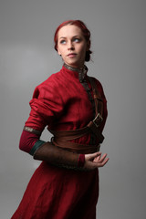 portrait of a red haired girl wearing medieval warrior outfit, studio background.