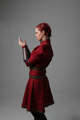 portrait of red haired girl wearing red medieval out fit, studio background.