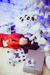 Charming girl lies on the floor under white Christmas tree with toy pandas
