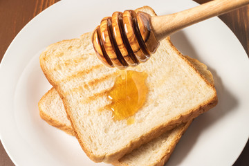 Honey with stick pouring over toast bread
