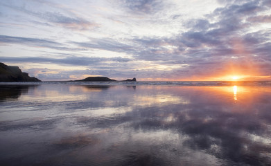 Landscape image of Rhossili Beach, South Wales at sunset with reflections 