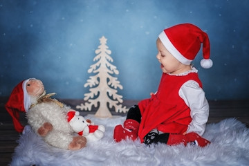 Baby girl in Santa hat sitting in a Christmas interior with toys.
