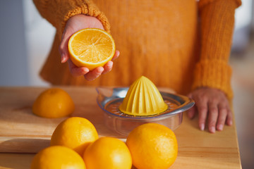 Mixed race woman squeezing orange fruit and making the juice while standing in modern kitchen
