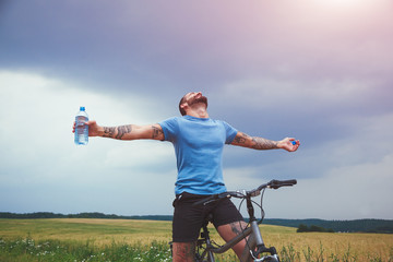 Happy man with bike spreading hands and drinking water resting. Freedom or happiness concept
