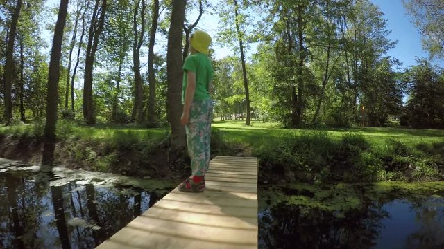 Little girl standing on footbridge in woods. Summer lifestyle moment of a happy childhood.